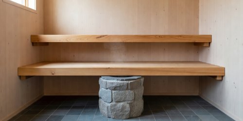 Two-tier thermally modified aspen sauna benches aligned above a cylindrical stone heater in natural light